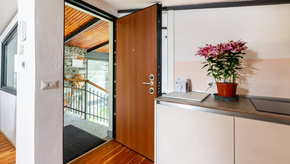 Welcoming entrance of La Casa degli Ulivi featuring wooden security door, parquet flooring and elegant details like fresh flowers - Independent access with garden view