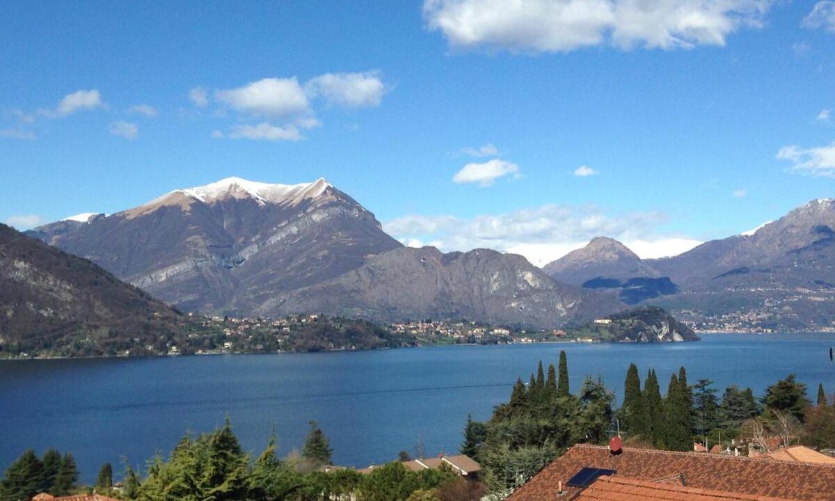 Vista panoramica sul Lago di Como dalla Casa degli Ulivi: montagne innevate, acque azzurre e cipressi secolari con Bellagio sullo sfondo