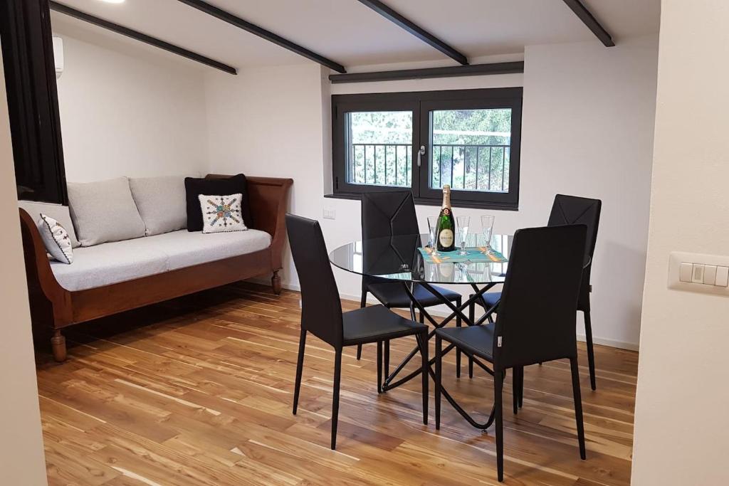 Soggiorno luminoso de La Casa degli Ulivi con divano elegante, tavolo da pranzo in vetro e parquet in legno naturale - Vista dalle finestre sul giardino di ulivi